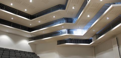 Auditorion katto, jossa lamppuja ja ikkunoista kajastavaa valoa.