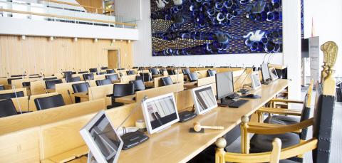 Tyhjä kaupunginvaltuuston istuntosali pöytine ja tuoleineen.