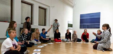 Opettaja ja lapsiryhmä kuuntelevat museo-opasta.