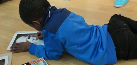 Lapsi makaa taidemuseon lattialla ja värittää kuvaa.