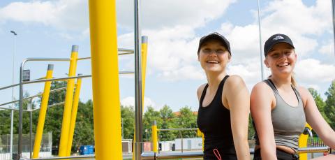 Kaksi henkilöä istuu treenilaitteen penkillä.