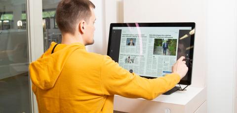 Asiakas lukee lehteä isolta kosketusnäytöltä.