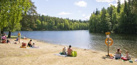 Ihmisiä uimarannalla istumassa hiekalla aurinkoisena päivänä.