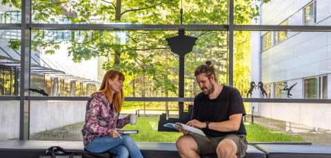 Opettaja ohjaa opiskelijaa koulun aulassa kielen opiskelussa.