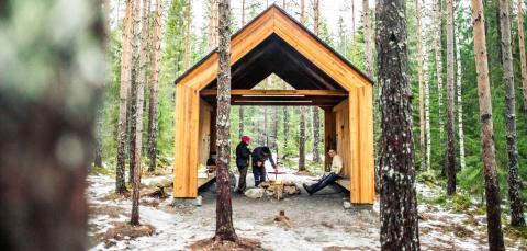 Kaksi ihmistä tekevät ruokaa ulkomajassa luonnon keskellä.