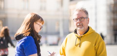 Sinipaitainen kaupungin työntekijä haastattelee tamperelaista kadulla.