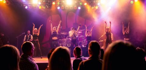 Yleisö seuraa musiikkiesitystä, jossa esiintyjät tanssivat.