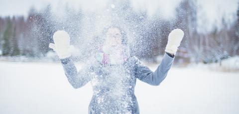 Nuori heittää lunta ilmaan talvisessa maisemassa