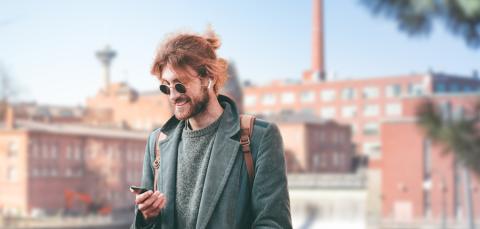 Henkilö seisoo Tammerkosken rannalla ja selaa älypuhelinta, taustalla koski ja Frenckellin rakennuksia sekä kaukana Näsinneula.