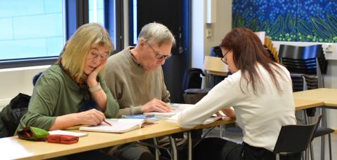 Kolme henkilöä opiskelee luokkahuoneessa pöydän ääressä.