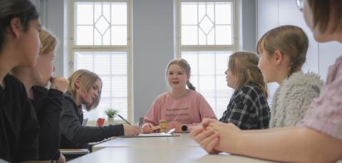Ryhmä lapsia istuu pitkän vaalean pöydän ääressä. 