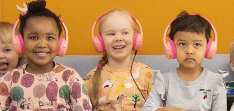 Seitsemän lasta istuu sohvalla, kolmella keskimmäisellä on kuulokkeet päässä.