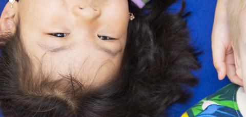 Kaksi lasta vierekkäin matolla. Toinen katsoo kameraan ja toinen sivulle.