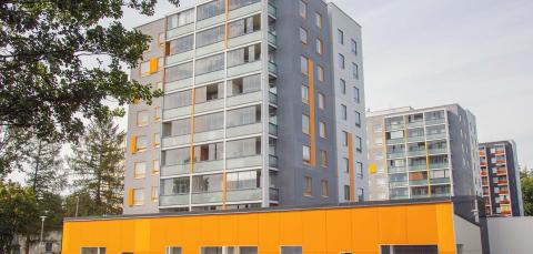 Kolme kerrostaloa, etualalla puu, nurmikkoa ja keltainen autokatos.