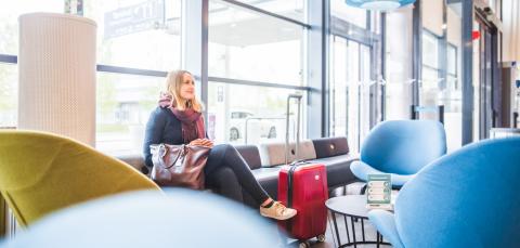 Henkilö istuu lentokentällä matkalaukun kanssa sohvalla.