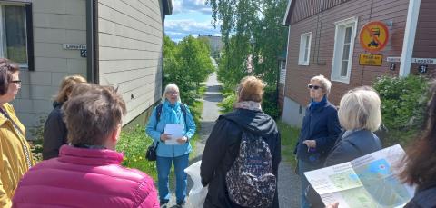 Luotsi ja luotsattavat seisovat puutalon edessä kadulla kesällä.