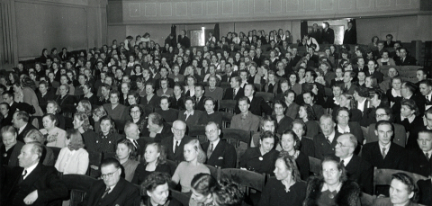 Henkilöistä suuressa luentosalissa, jonka takana on parvi.