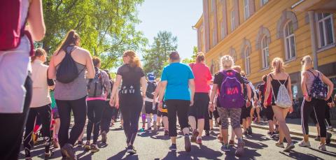 Suuri joukko ihmisiä kulkemassa kadulla samaan suuntaan aurinkoisena päivänä.