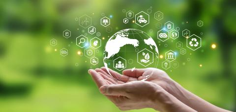 Kädet pitävät pientä maapalloa, jonka ympärillä on erilaisia symboleita, kuten sähköauto, CO2 ja kehää kiertävät nuolet.