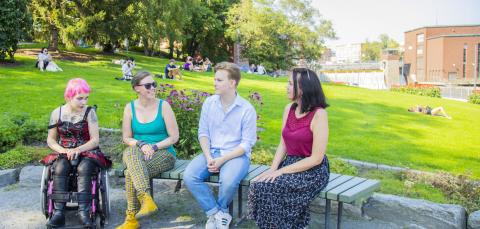 Ihmisiä istuu Koskipuistossa penkillä, takana nurmella istuskelee muitakin ihmisiä.