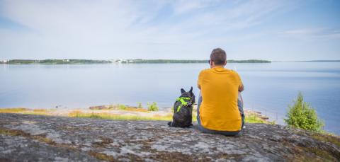 Mies ja hänen koiransa istuvat selin kameraan katsellen järvelle.