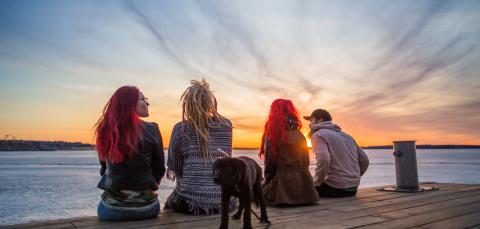 Ihmisiä laiturilla järven rannalla katselemassa auringonlaskua.