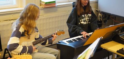 Kaksi oppilasta soittavat. Toinen soittaa sähkökitaraa, toinen koskettimia.