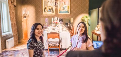 Kaksi tummahiuksista nuorta naista katsoo museonäyttelyä vanhoilla huonekaluilla sisustetussa tilassa.