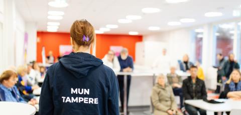 Mun Tampere -huppariin pukeutunut kaupungin työntekijä on yleisön edessä keskustelemassa heidän kanssaan.
