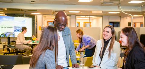 Neljä hymyilevää, eri etnisiä ryhmiä edustavaa ihmistä keskustelemassa pöydän ääressä.