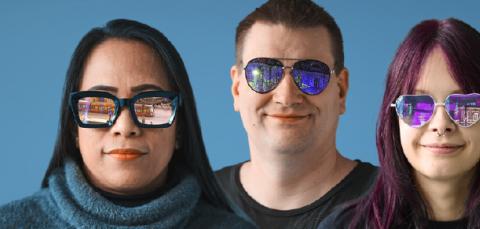 Neljä erilaista ihmistä katselee kohti. Heistä kaikilla on aurinkolasit, joista heijastuu erilaisia kaupunkiin liittyviä näkymiä.