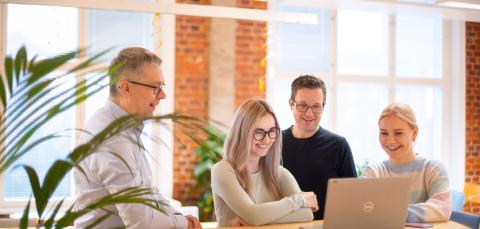 Neljä henkilöä katsoo tietokonetta.