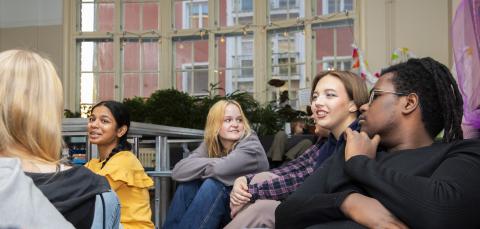 Nuoria henkilöitä istumassa sohvilla, taustalla ikkuna.