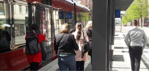 Ihmisiä kävelemässä ratikkapysäkillä. Ratikka on pysäkillä pysähtyneenä.