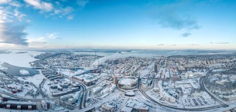 Ilmakuvassa levittäytyy luminen Tampere. Keskellä Nokia Arena ja risteilevät tiet, taustalla järvet ja sininen taivas.