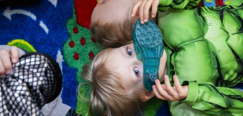 Lapsi makaa lattialla naamiaisasussa ja pitelee kasvojen edessä kenkää.