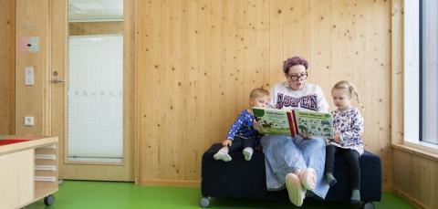 Aikuinen lukee kirjaa kahdelle lapselle.