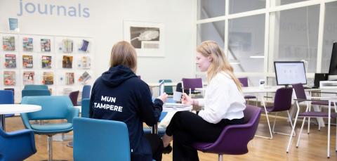 Kaksi henkilöä istuu Koilliskeskuksen kirjastossa pöydän ääressä.