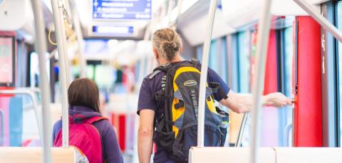 Kaksi henkilöä reput selässä matkustamassa ratikalla.
