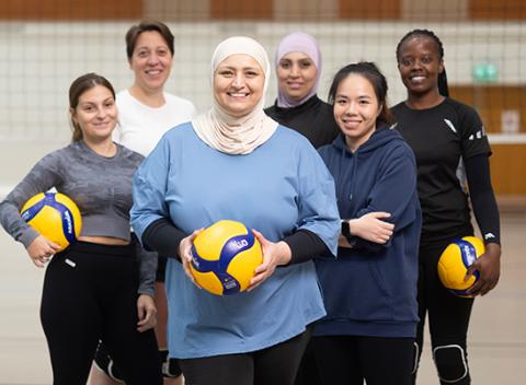 Kuusi naista lentopallokentällä. Kaikki katsovat kameraan ja hymyilevät. 