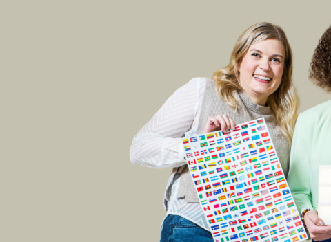 Kolme henkilöä seisoo vierekkäin. Heillä on käsissään kielten opiskelutavaroita, kuten lippuja ja taulu.