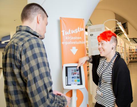 A library staff member instructs a client on how to use e-services from the screen.