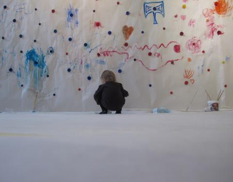 Pieni tyttö maalaa seinään vesivärillä.