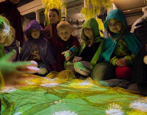 Lapset istuvat vihreän leikkilammen ympärillä.