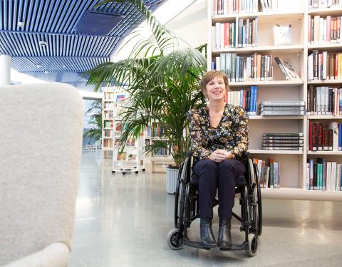Henkilö istuu pyörätuolissa kirjahyllyjen edessä kirjasossa.