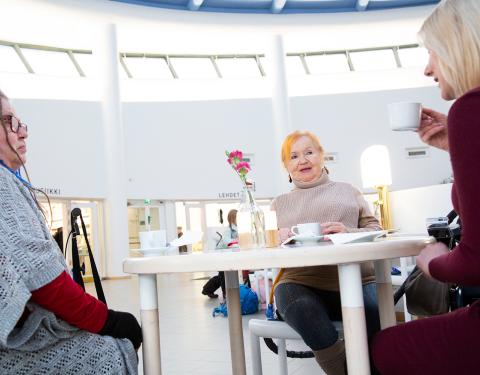 Kolem henkilöä istuu pöydän ympärillä kahvittelemassa pääkirjasto Metson valoisassa kahvilassa.