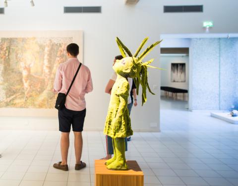 Henkilö katselee maalausta. Takana teos lapsihahmosta.