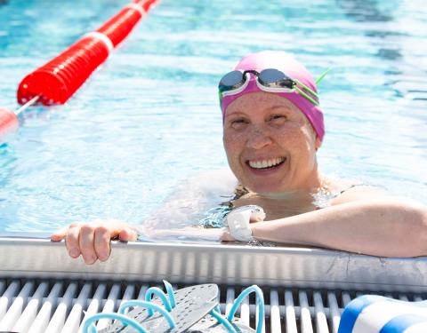 Hymyilevä henkilö kesällä maauimalassa. Aurinko paistaa.