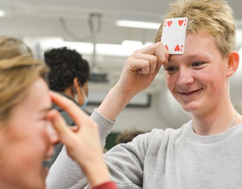 Kaksi kahdeksasluokkalaista pitää iloisin ilmein pelikortteja otsallaan draamallisessa pelissä .