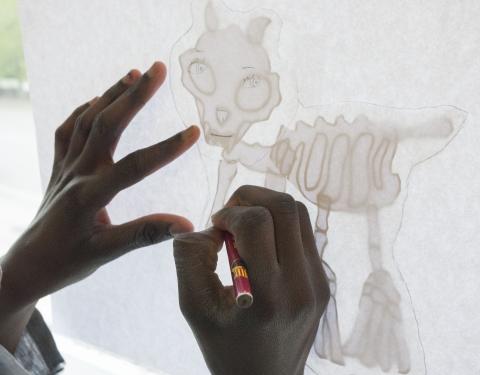 Kaksi kättä lähikuvassa, taustalla piirretty hahmo. Henkilö täydentää kuvaa omalla piirroksellaan.